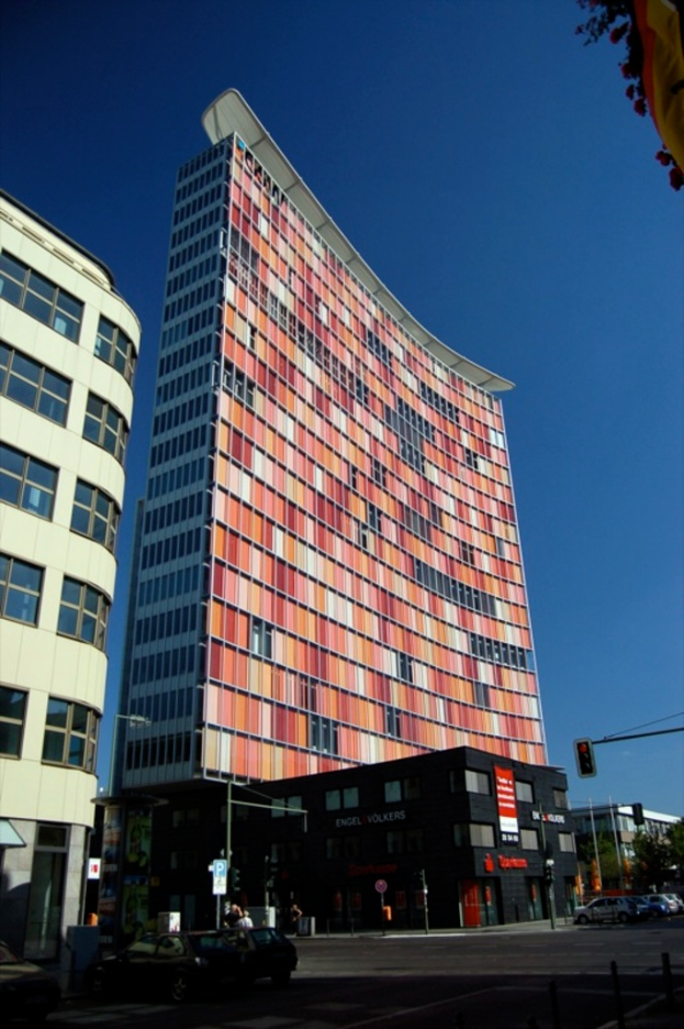 Hohe Gebäude mit parkenden Autos in einer Parkfläche und ein Verkehrssignalpfahl auf der rechten unteren Seite.