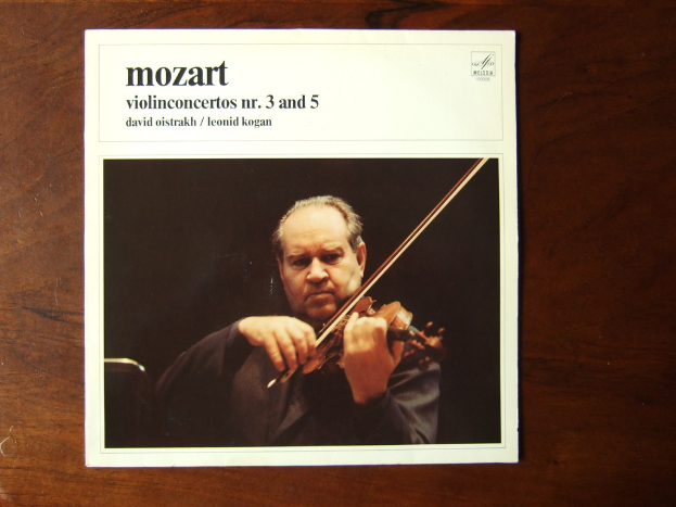 Ein Mann in einem schwarzen Mantel spielt Geige auf einem Holztisch, mit einem schwarzen Hintergrund und einem kleinen Zitat oben auf dem Bild.