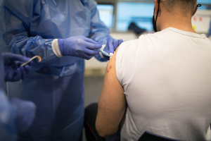 Ein Mann in einem weißen Hemd erhält eine Impfung von einem Arzt in einem blauen Kleid und Handschuhen, der eine Spritze hält, mit einem unscharfen Hintergrund.