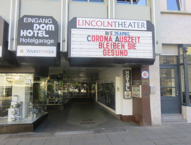 Das Lincoln Theater in Berlin, Deutschland, mit Glasfenstern und -türen und einer Texttafel außen sowie einer belebten Stadtkulisse im Inneren.