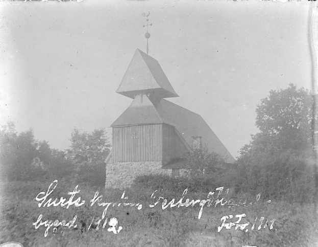 Schwarzes und weißes Foto der Kirche des Heiligen Grabes mit einem Turm, umgeben von Bäumen und Pflanzen unter einem bewölkten Himmel.
