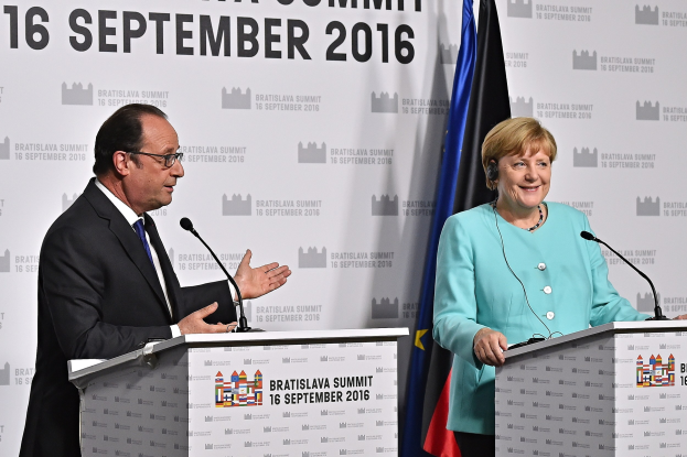 Bundeskanzlerin Angela Merkel und Frankreichs Präsident François Hollande lächeln auf dem Bratislava-Gipfel 2016, vor Podien mit Mikrofonen und einem Banner mit der Aufschrift "Bratislava-Gipfel 2016".