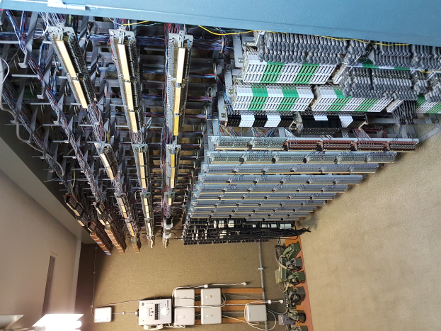 Ein großer Raum voller numerous wires und elektronischer Geräte, einschließlich Servern und Kabeln, die miteinander verbunden sind, mit einer Wand auf der linken Seite, die einem Rechenzentrum ähnelt.