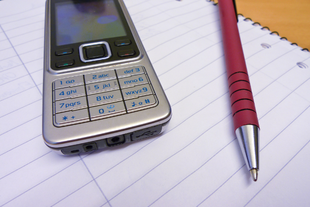 Ein Mobiltelefon und ein Stift liegen auf einem offenen Buch.