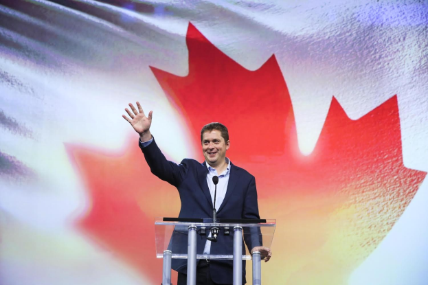 Kanadischer Premierminister Alex Salmond spricht an einem Rednerpult mit Mikrofonen vor einer kanadischen Flagge und einem Bildschirm.