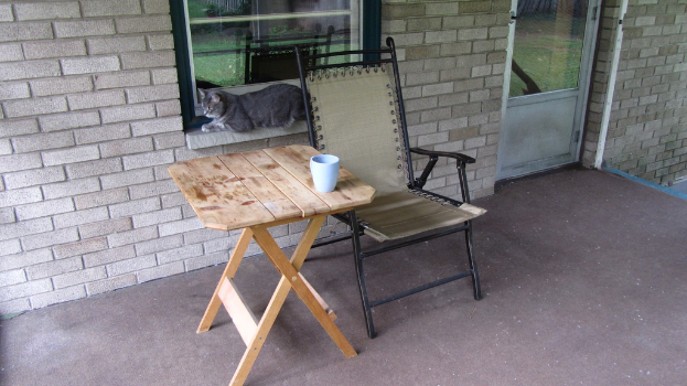 Ein Haus von außen mit einer Katze, einem Stuhl und einem Tisch in der Mitte und einer Tür oben rechts.