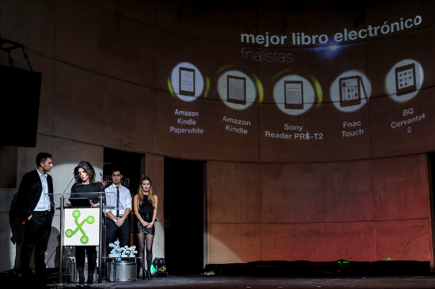 Vier Personen auf der linken Seite, wobei eine Frau einen Vortrag hält und im Hintergrund Bilder von Gadgets mit ihren Namen darunter zu sehen sind.