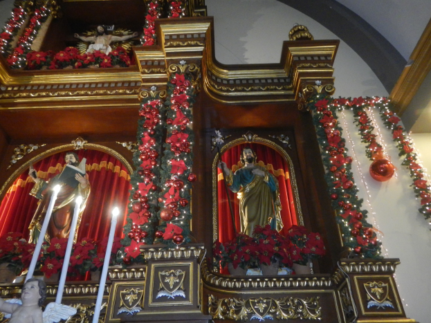 Kirchaltar für Weihnachten mit Statuen, Kerzenleuchtern, Blumenbouquets und Dekoartikeln geschmückt, mit Treppe nach oben führend.