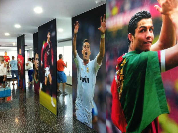 Ein Banner mit dem Fußballspieler Rolando, mit Menschen links neben einem Tisch und Lichtern oben.