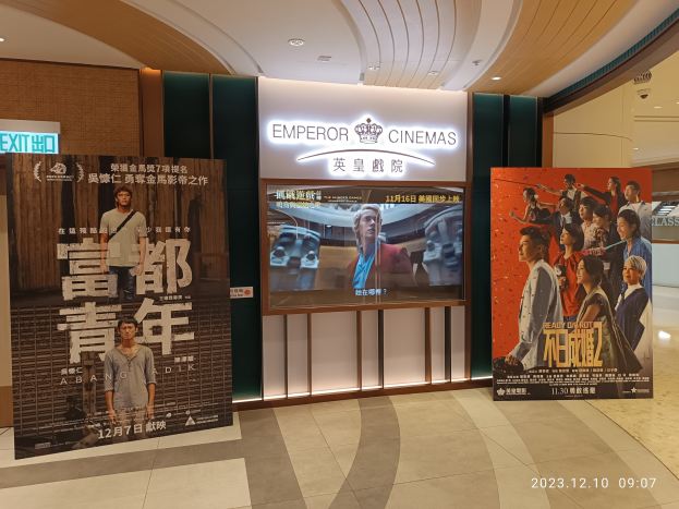 Eintritt zum Kaiser-Kinos in Hong Kong mit Bannern, einem Bildschirm, einer Namensanzeige, Deckenleuchten und einem Wasserzeichen.