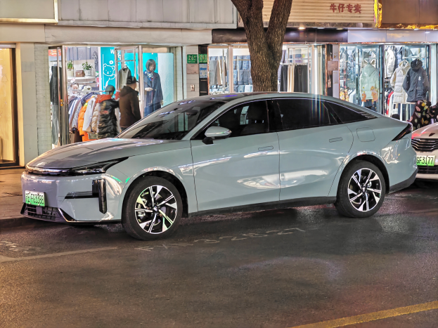 Ein Mitsubishi Lancer EV auf einer nächtlichen Straße geparkt, umgeben von Gebäuden, Geschäften, Schaufensterpuppen, Schildern und Lichtern.