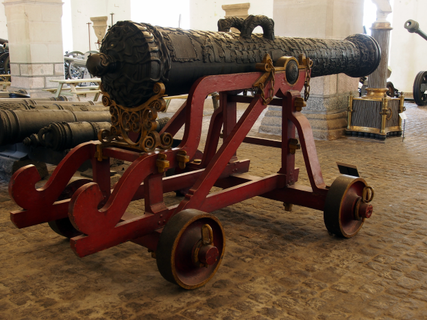 Ein alter Kanone in einem Museum ausgestellt, umgeben von anderen Kanonen und Säulen im Hintergrund.