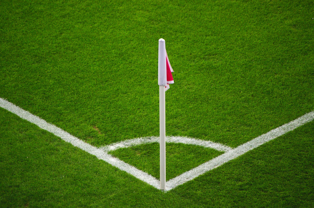 Ein Fußballfeld mit grünem Rasen, weißen Begrenzungslinien und einem weißen Pfosten mit einer roten und weißen Flagge auf dem zentralen Strafstoßpunkt.