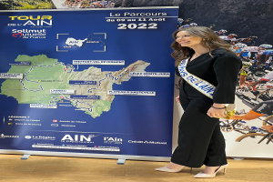 Eine Frau steht vor einer Fahne mit einer Karte von Frankreich, auf der ein Band mit der Aufschrift "Tour de France 2020" zu sehen ist.