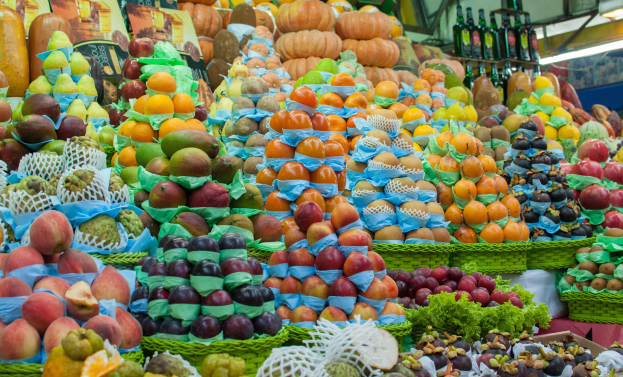 Ein Marktstand mit Äpfeln, Orangen, Birnen und anderen Obst- und Gemüsesorten, mit Flaschen auf Regalen und Deckenbeleuchtung.