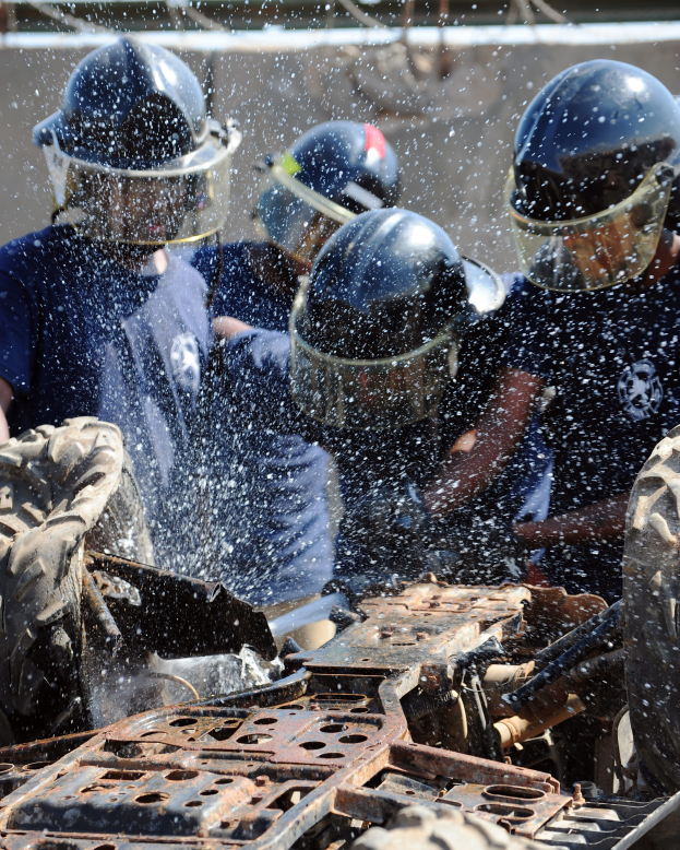 Eine Gruppe von Polizisten in blauen Uniformen und Helmen sprüht sich gegenseitig Wasser vor einem Fahrzeug, mit einer Wand im Hintergrund.