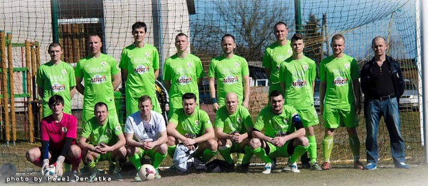 Mannergruppe in grünen T-Shirts auf einem Fußballfeld mit Ball und Tor im Hintergrund.