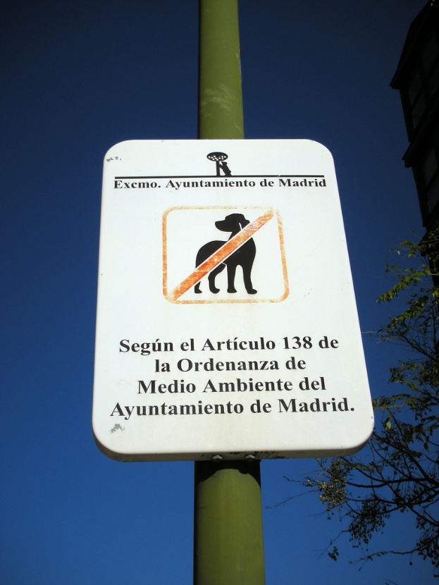 Ein an einem Pfahl befestigtes Schild mit Bäumen, Gebäuden und Himmel im Hintergrund.