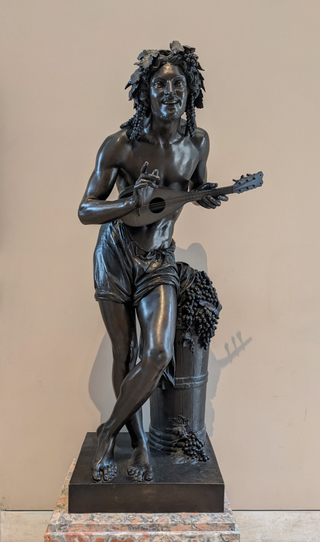 Bronzestatue eines Mannes, der eine Gitarre spielt, mit einer Wand und einem Boden im Hintergrund.