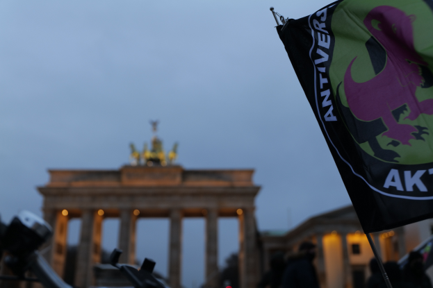 Eine Gruppe von Menschen steht vor dem Reichstagsgebäude in Berlin, Deutschland, mit einer Fahnenstange, die ein Logo und Text trägt, versammelt, um gegen die antifaschistische Bewegung zu protestieren.