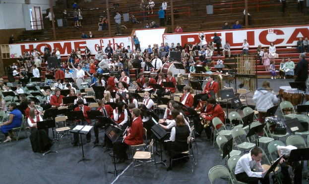 Eine Gruppe von Kindern sitzt auf Stühlen in einem Stadion während eines Musikunterrichts, mit sichtbaren Stadionplätzen im Hintergrund.