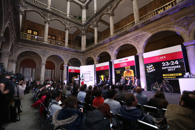 Eine Gruppe von Menschen sitzt an einem Tisch mit einem Podium und einem Mikrofon vor einer Menge, Kameras und Bannern während einer Pressekonferenz für das CDMX 2017-Event.