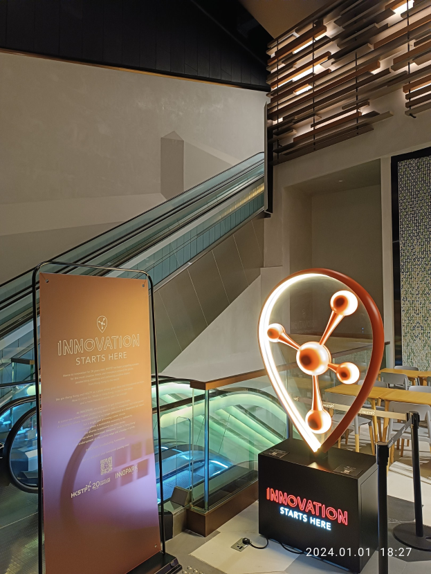 Großes Schild in einem Gebäude mit einer Rolltreppe im Hintergrund, mit "Innovation Starts Here" auf einer Tafel links und Tischen mit Stühlen rechts, was auf die HSTP20 Expo hinweist.