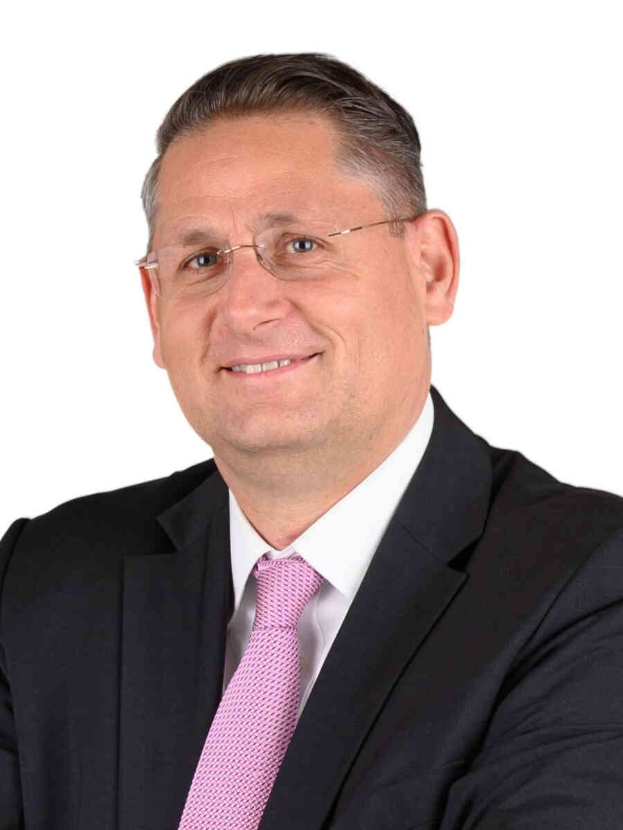 Ein Mann im Anzug und mit Krawatte, der eine Brille trägt, lächelt in die Kamera vor einem weißen Hintergrund, was darauf hinweist, dass er ein Finanzberater ist.