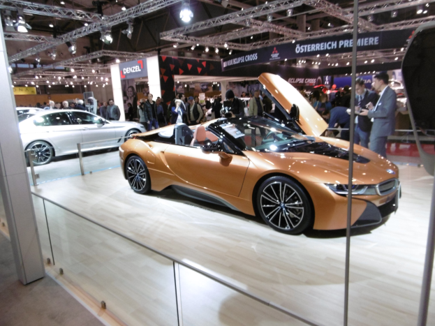 Ein schickes schwarzes BMW i8 Cabrio mit Chromakzenten auf der Frankfurt Motor Show umgeben von formell gekleideten Gästen in einer Atmosphäre der Aufregung.