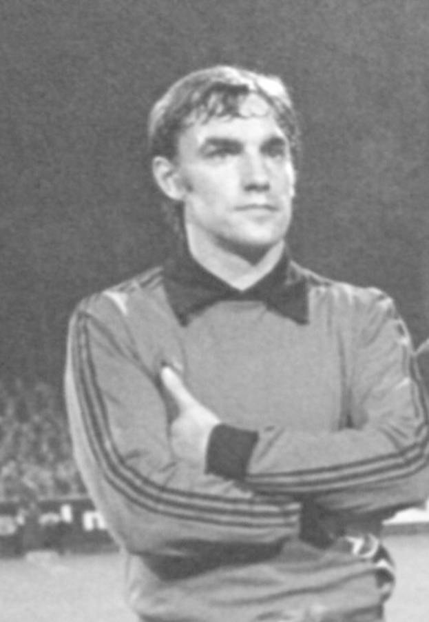 Schwarzes und weißes Foto eines Mannes auf einem Fußballfeld mit verschränkten Armen, umgeben von sitzenden Zuschauern, der legendäre Manchester United-Torwart, der im Alter von 89 Jahren starb.