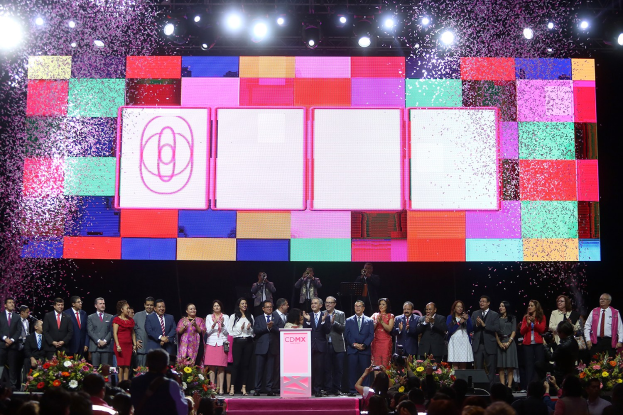 Gruppe von Menschen auf einer Bühne mit einem Podium, Blumengestecke auf beiden Seiten, Kameras in der Hand und ein großer Bildschirm mit Lichtern im Hintergrund während der Eröffnungszeremonie des 2018 China International Film Festival.