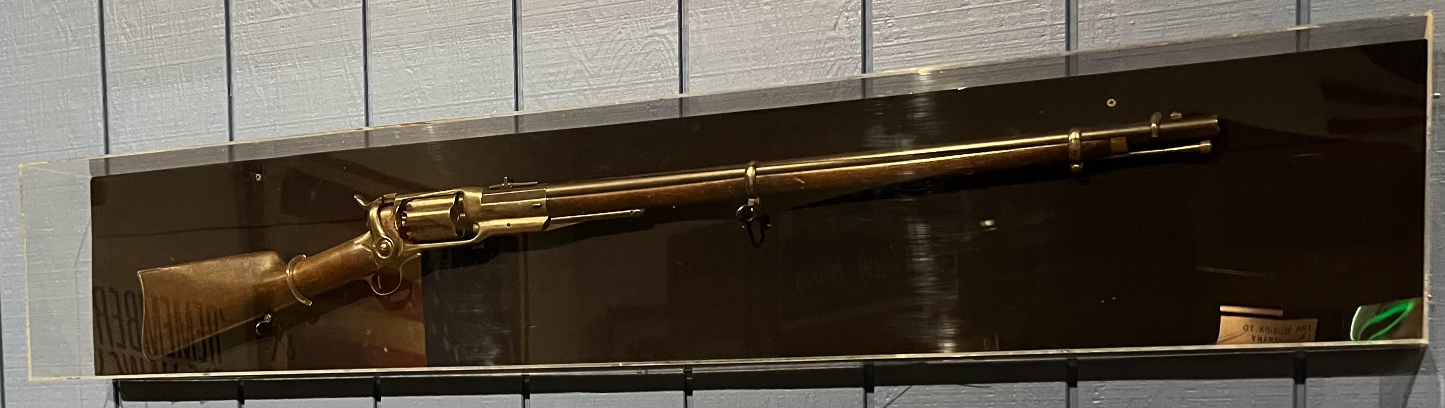 US Springfield Model 1873 Einzelladerrepetierer mit messingbeschichtetem Finish und Holzschaft, ausgestellt in einer Glasvitrine mit einem messingbeschichteten Abzugbügel.