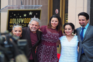 Gruppe von Menschen, die vor einem Hollywood Walk of Fame Star posen, mit einem Podium, Mikrofon und einer Tafel mit Text dahinter, einer Person mit einer Kamera links und einer Tür im Hintergrund.