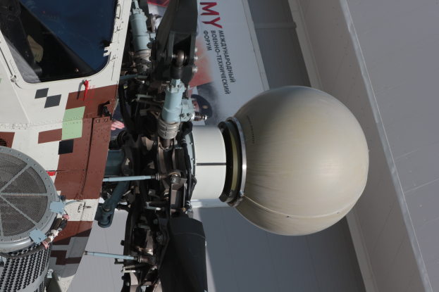 Ein Nahaufnahme einer zylindrischen Rakete mit spitzem Ende auf einer Ausstellung vor einem Gebäude, mit sichtbarem Text an der Wand im Hintergrund.