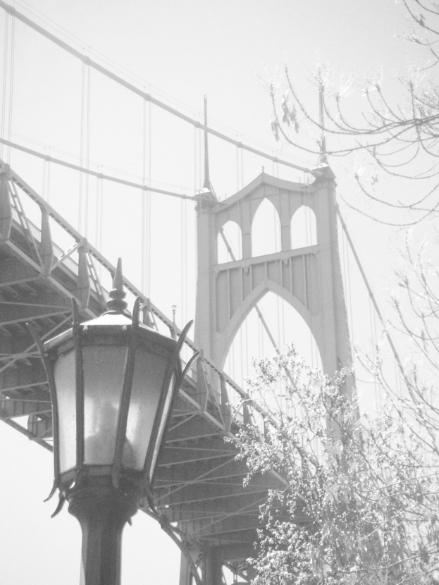 Ein altes Bild einer Hängebrücke mit einem schwarzen Laternenpfahl im Vordergrund und einem Baum in der rechten Ecke.