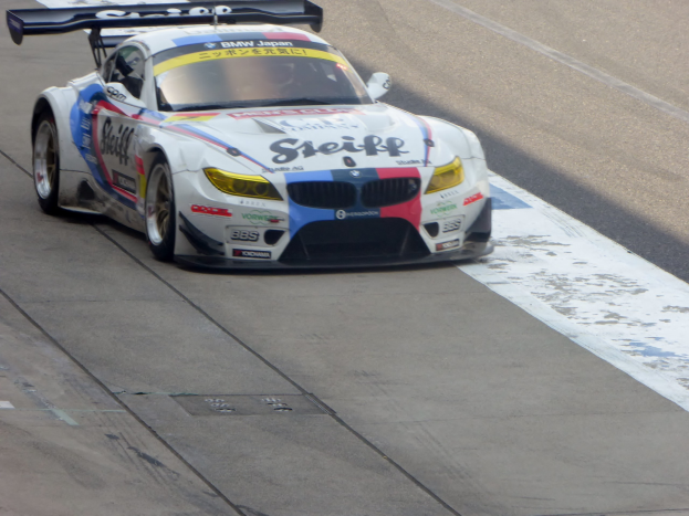 Ein strahlend blauer und weißer BMW Z4 GT3 Rennwagen mit großen glänzenden Rädern, der auf einer Rennstrecke fährt.