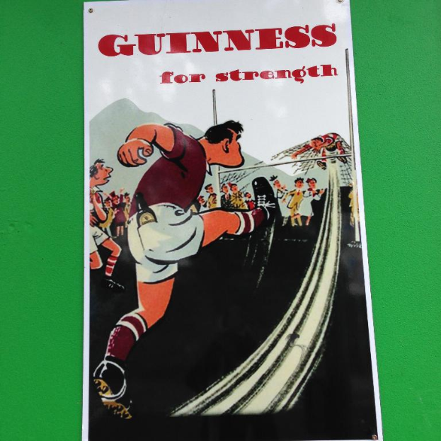 Ein Cartoon-Poster mit Menschen, die auf dem Boden stehen und eine Person an einem Netz h├Ąngt, mit dem Text "Guinness f├╝r St├Ąrke" darauf.