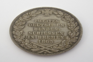 Eine Silbermünze mit der Aufschrift "Zweites Deutsches Bundes Schießen in Bremen" vor einem weißen Hintergrund.
