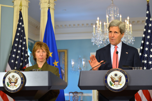 Außenminister John Kerry und der Minister für Innere Sicherheit stehen an Podien im East Room des Weißen Hauses, Kerry spricht in ein Mikrofon, zwei Flaggen im Hintergrund und eine Kristallleuchte